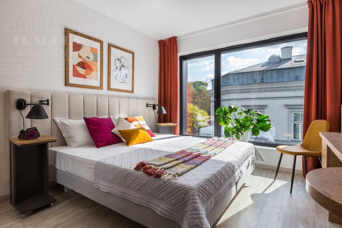 Ein modernes Schlafzimmer mit einem großen Bett, einem Schreibtisch, einem Sessel, einem Topfpflanzen und einem Fenster mit Vorhängen.