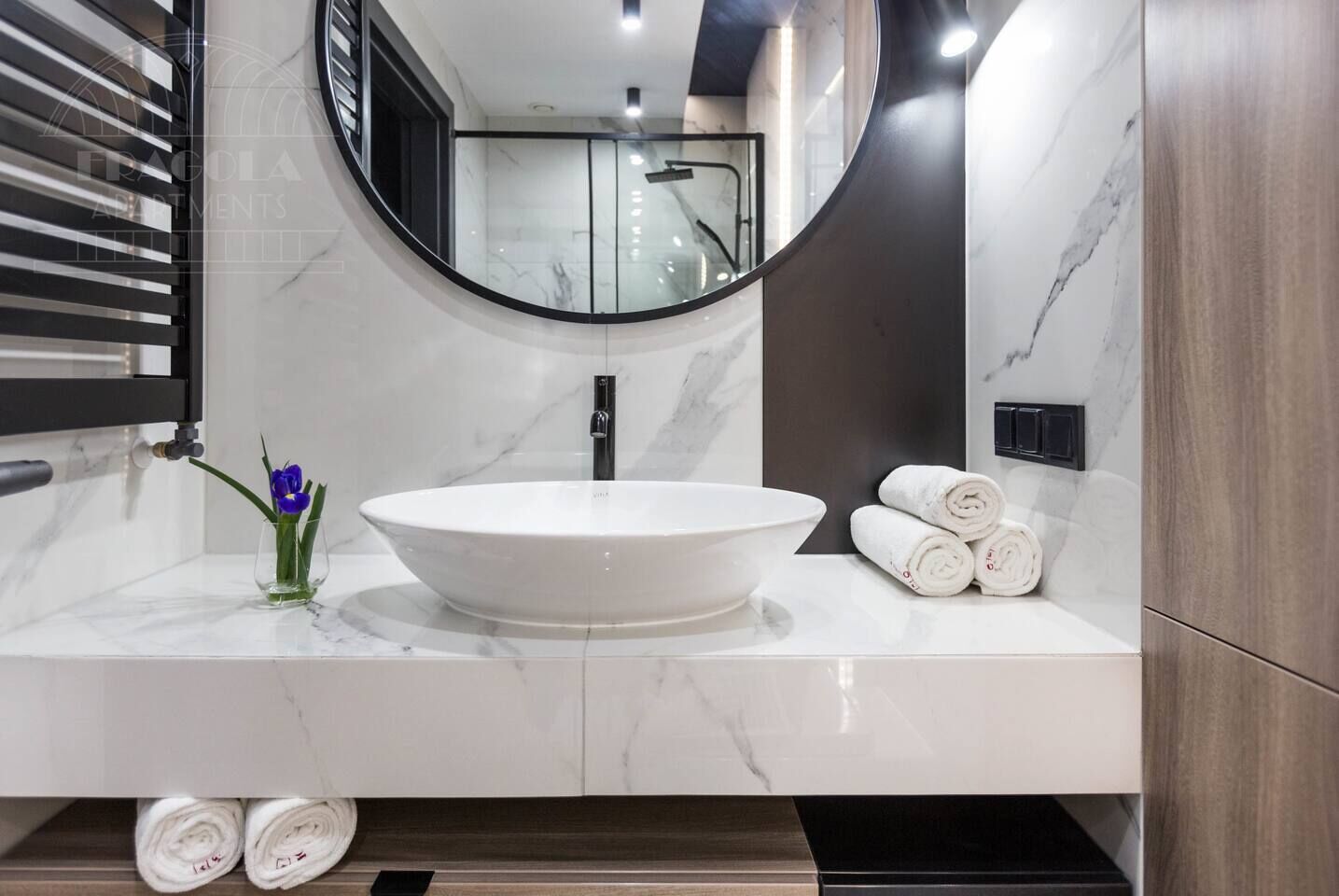 A modern bathroom with a large oval sink, a round mirror, and a towel rack.