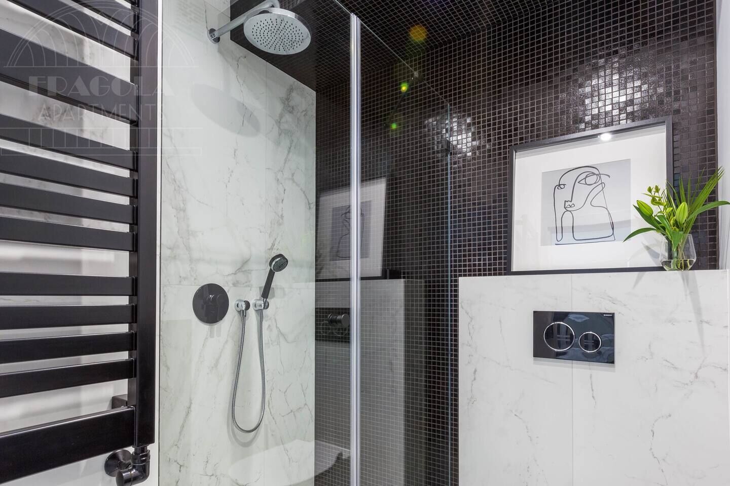 Une salle de bain moderne avec une douche à l’italienne en verre, un mur en marbre, un miroir à cadre noir et une petite plante en pot.