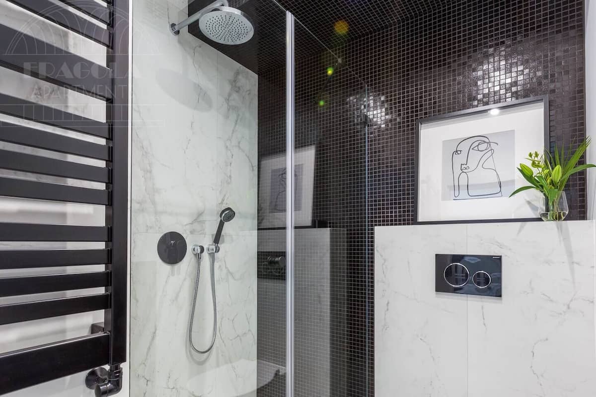 Une salle de bain moderne avec une douche Ă lâitalienne en verre, un mur en marbre, un miroir Ă cadre noir et une petite plante en pot.