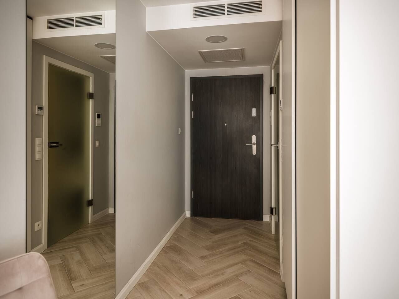 Ein Korridor mit Holzboden, einer dunklen Tür und einer hellen Wand.
