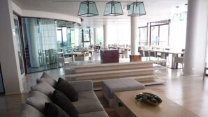 A spacious lobby with a modern design, featuring a grey sectional sofa, a wooden coffee table, and a glass wall providing a view of the dining area. - Teddy Bear Villa Hua Hin 2 (Cha-am)