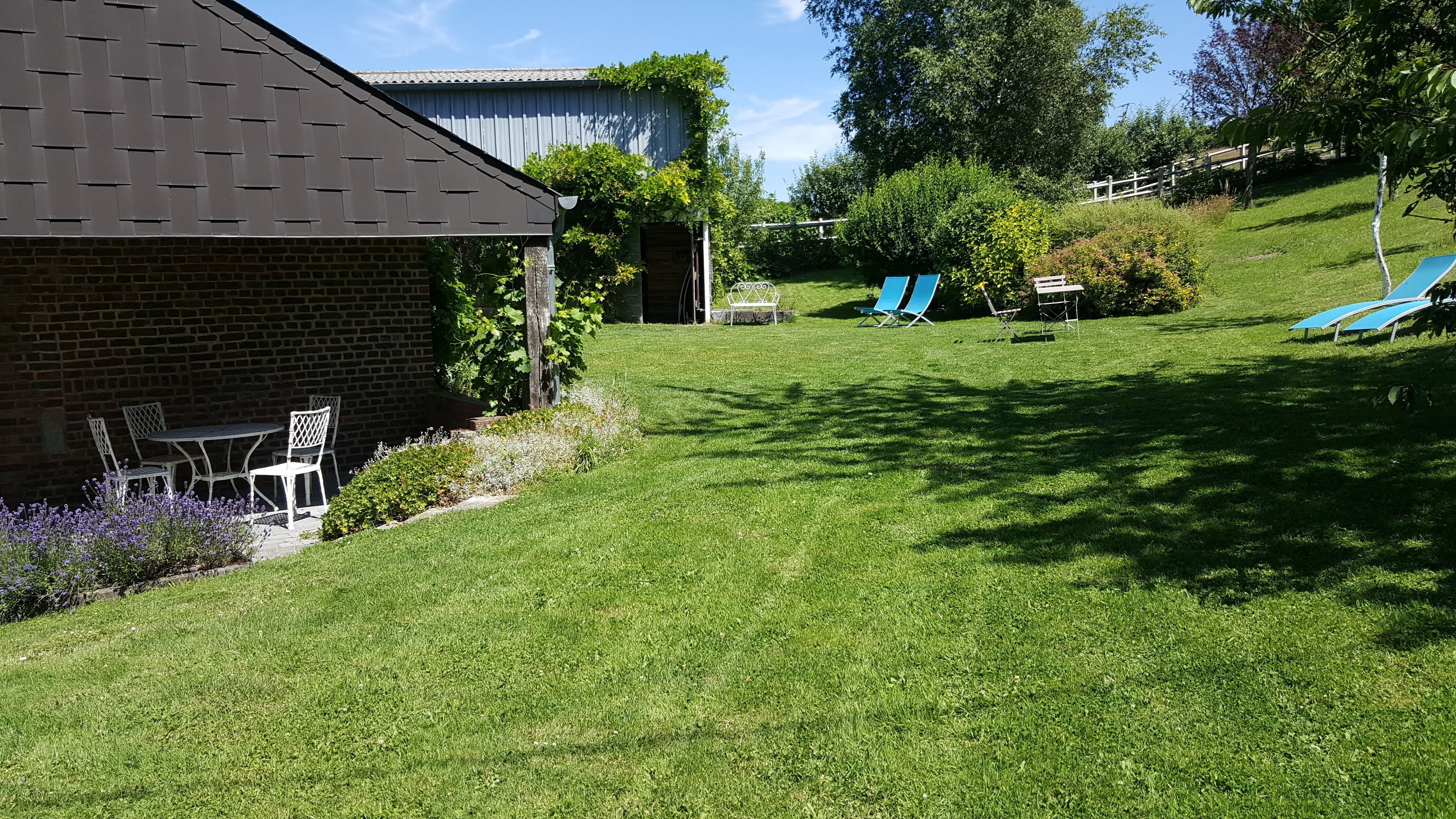 A grassy backyard with a brick house, a small patio with chairs, and a blue lawn chair.