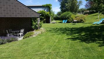 A grassy backyard with a brick house, a small patio with chairs, and a blue lawn chair.