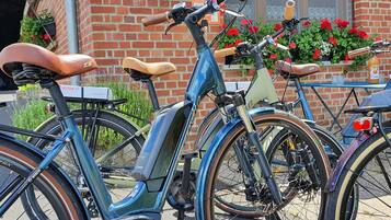 En række cykler parkeret foran en bygning med en murstensfacade og forskellige skilte.