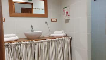 A bathroom with a wooden vanity, a white sink, and a mirror above it. There are towels stacked on the vanity and a small sign on the wall.