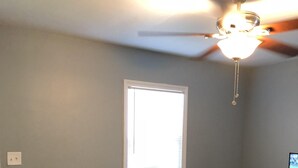 Ein Wohnzimmer mit einem dunkelbraunen Ledersofa, einem Glastisch, einem Deckenventilator und einem Fenster mit Jalousien.