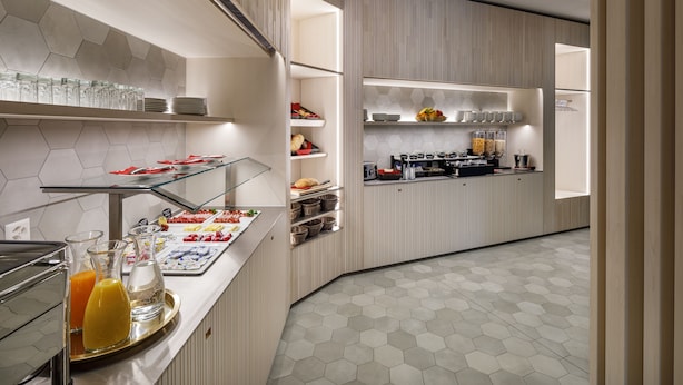 Un espace moderne dédié au petit-déjeuner, avec un sol carrelé à motifs hexagonaux, des plateaux de service en verre et des aliments disposés de manière soignée.