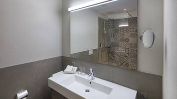 A modern bathroom with a large sink, a mirror, and a shower area.