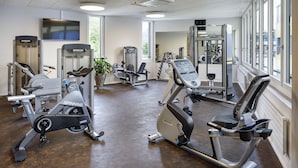 Une salle de sport équipée de divers appareils d’exercice, dotée de grandes fenêtres et d’un téléviseur fixé au mur.