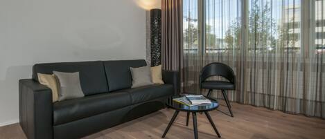 Una sala de estar moderna con un sofá negro, una mesita redonda y una silla negra.