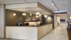 Un espace d'accueil au design moderne, comprenant un comptoir de réception, un bar et un coin salon avec des fauteuils.