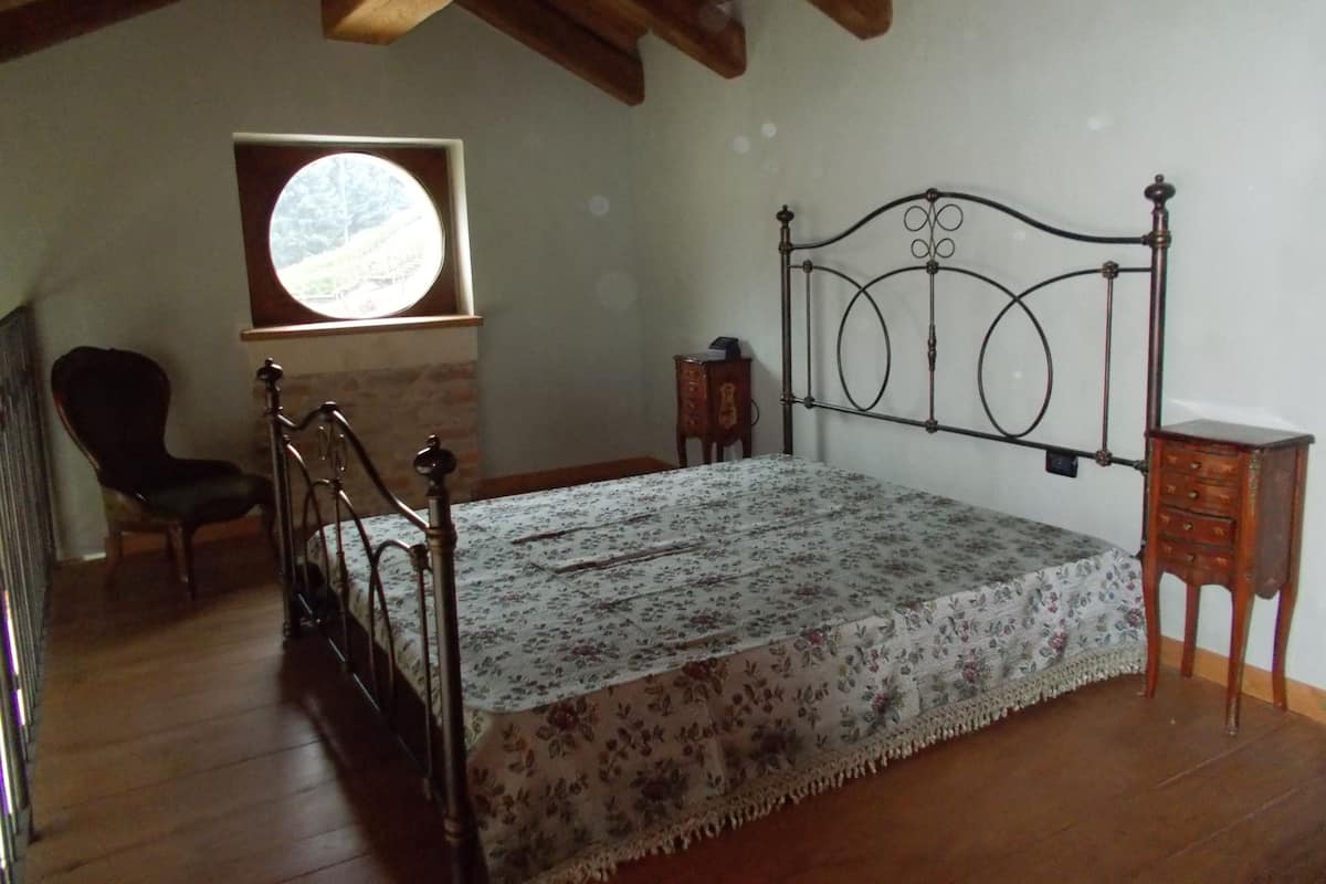 Une chambre avec un plancher en bois, un cadre de lit en métal, une petite table de chevet et une fenêtre donnant sur l’extérieur.