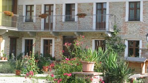A two-story building with a stone facade, multiple balconies with flower boxes, and a garden area with potted plants and flowers.