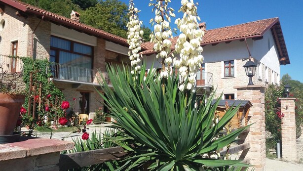 A stone building with a tiled roof, a balcony, and a garden with large white flowers and red roses.