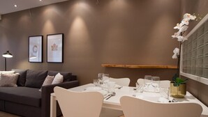 A modern dining area with a white table set for four, surrounded by white chairs. There is a sofa and a lamp in the background. - 2ndhomes Kamppi Center Apartment (Helsinki)