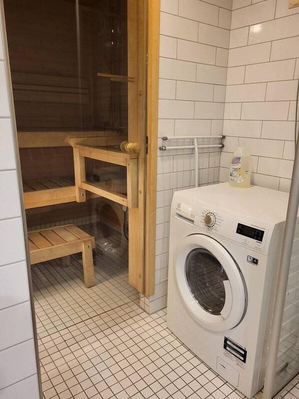 A laundry area with a washing machine, wooden shelves, and a tiled floor.