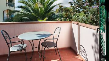 Un balcon avec une table et deux chaises, entouré d’un petit muret et d’un portail vert.