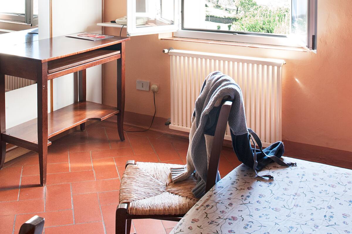 A room with a wooden desk, a chair, a radiator, and a window with an open door.