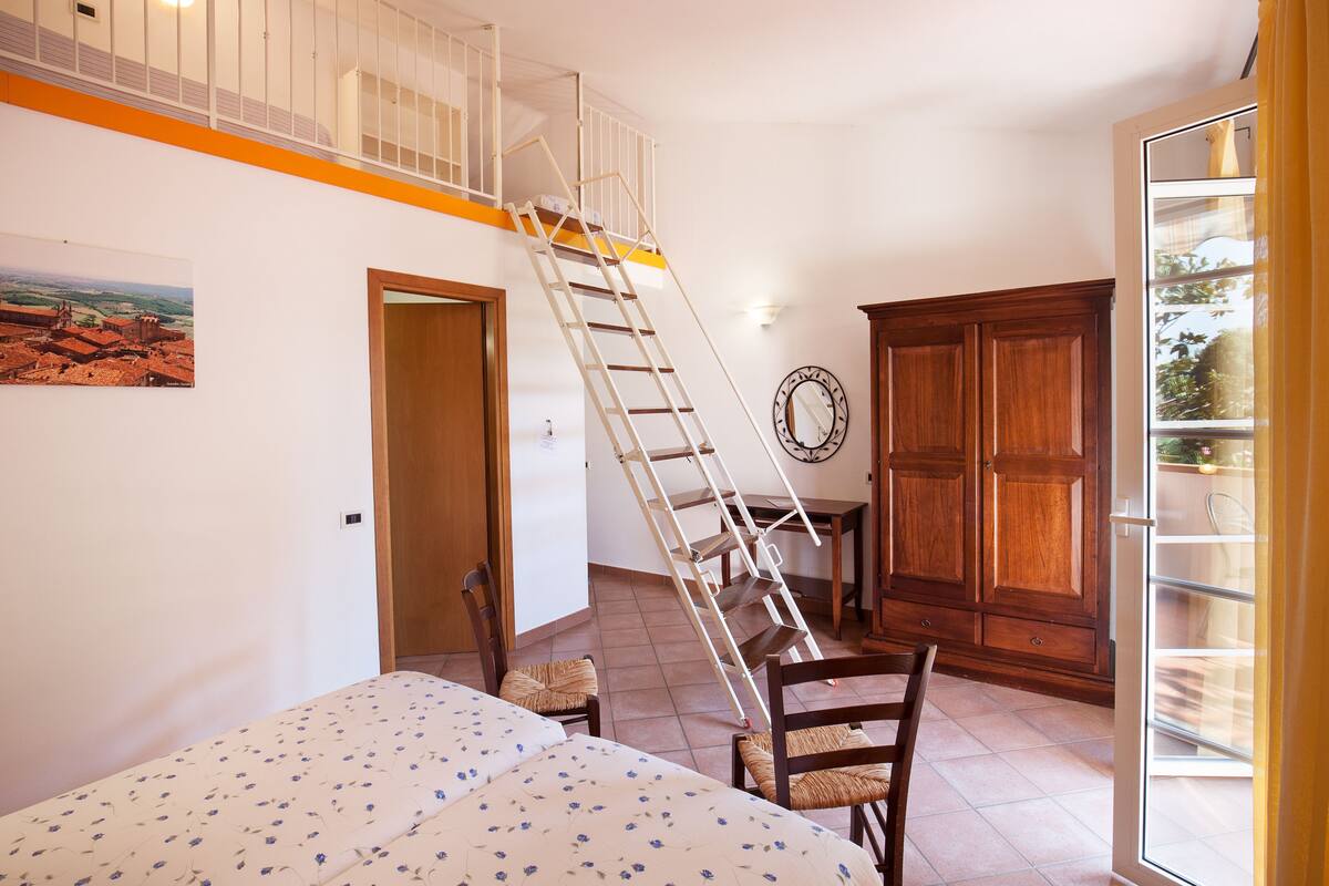 A bedroom with a bed, a wooden wardrobe, a ladder, a chair, and a door.