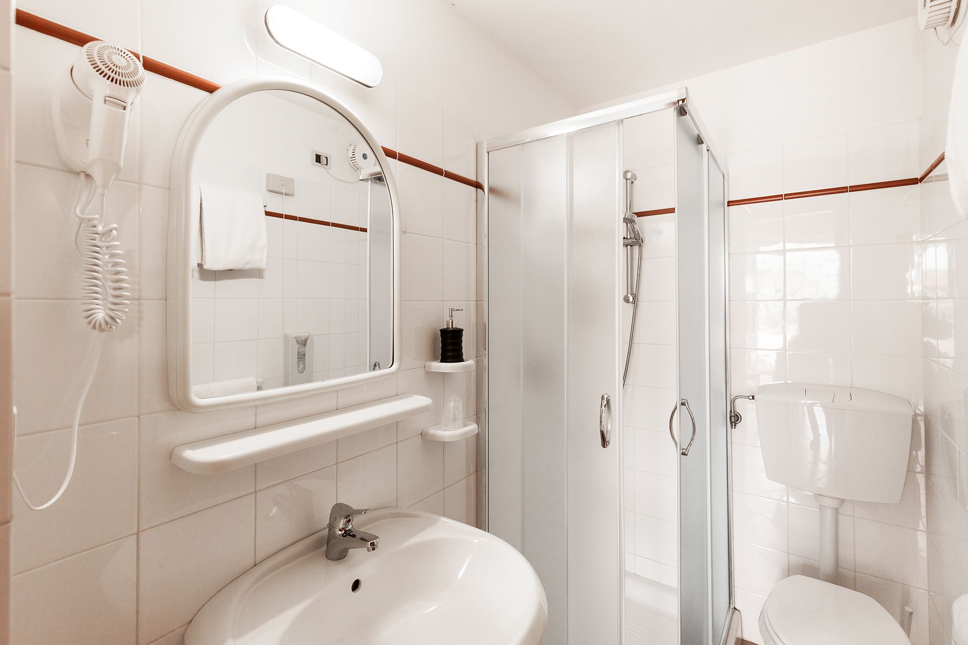 Ein modernes Badezimmer mit Waschbecken, Spiegel, Fön, Dusche und Toilette.