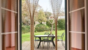 Un patio con mesa y sillas, vista a un jardín y un edificio al fondo.