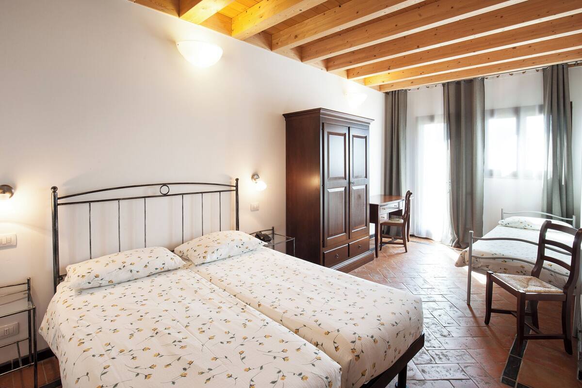 A bedroom with a double bed, a wooden wardrobe, a desk, and a chair.