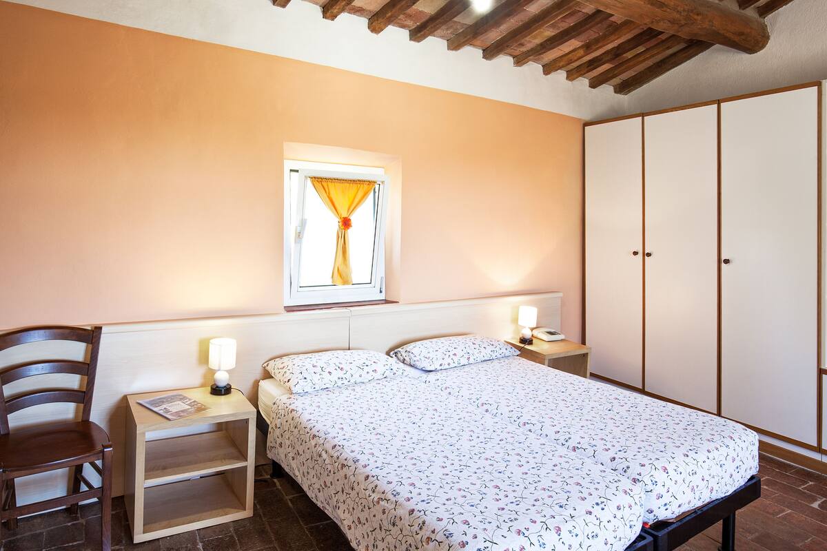 A bedroom with a bed, nightstand, chair, wardrobe, and a window with curtains.