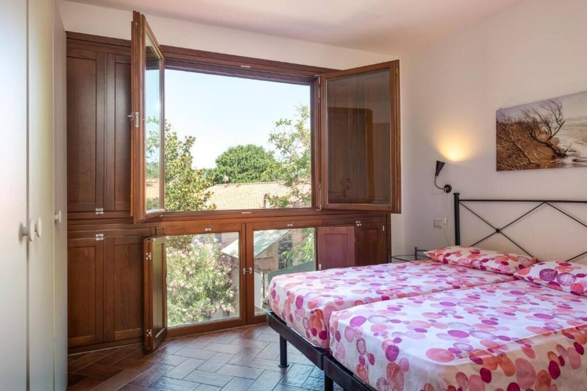 A bedroom with a large window, a bed with a floral bedspread, and wooden cabinets.