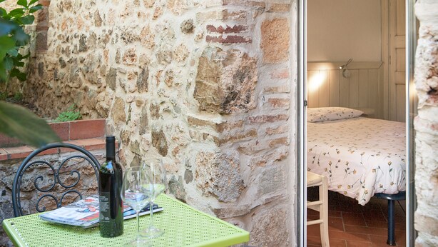 Una pared de piedra, una cama con edredón floral y una mesa con botella y vaso.