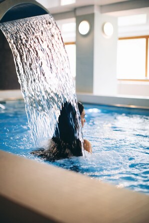 A person in a swimming pool with water flowing from a high point into the pool.