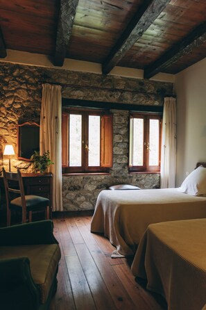 A rustic room with stone walls, wooden beams, a bed, a desk, and a chair.