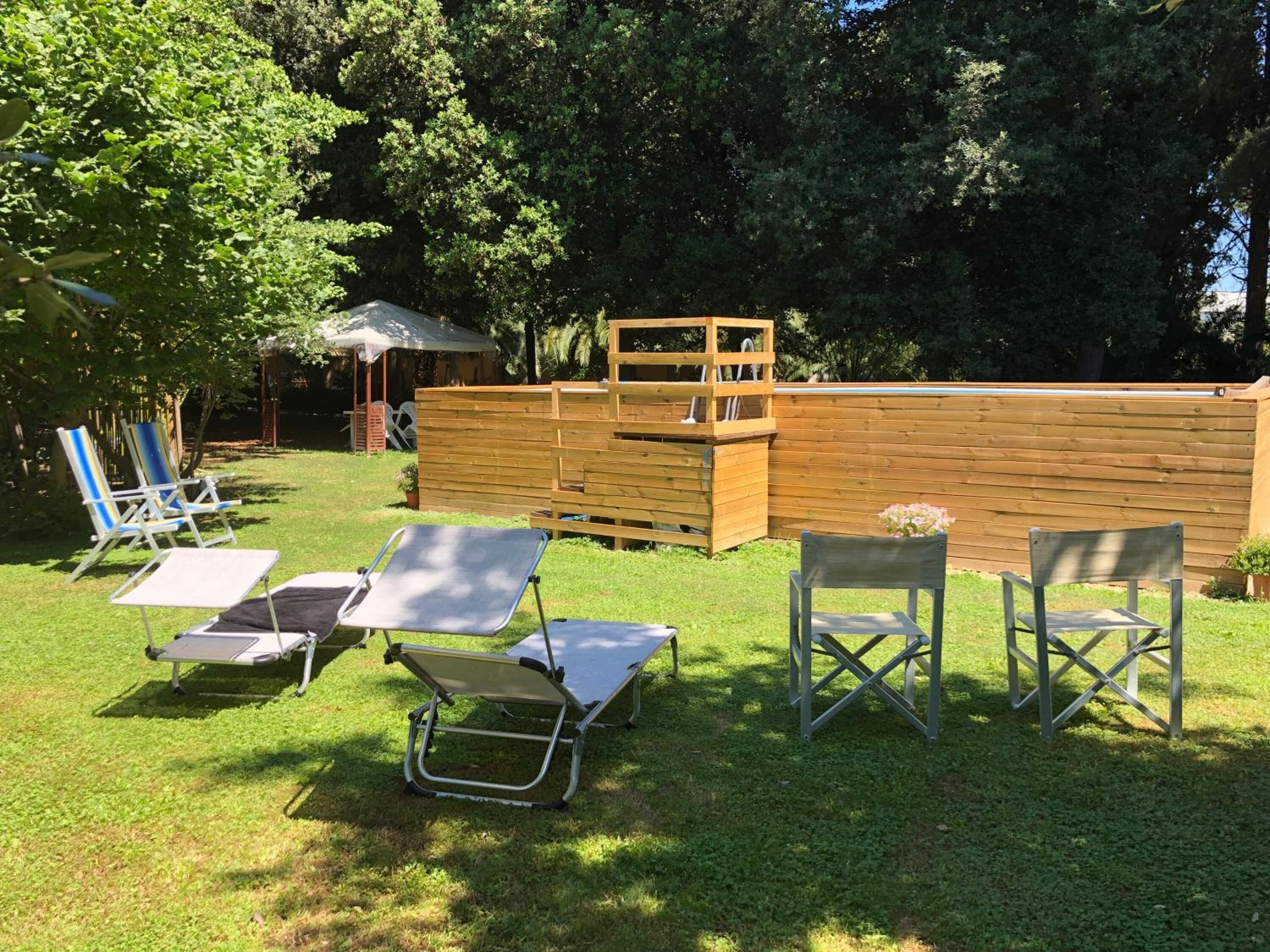 Ein Garten mit einer Holzterrasse, einem kleinen Tisch und mehreren Liegestühlen.