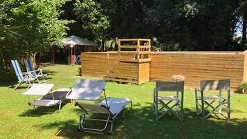Ein Garten mit einer Holzterrasse, einem kleinen Tisch und mehreren Liegestühlen.