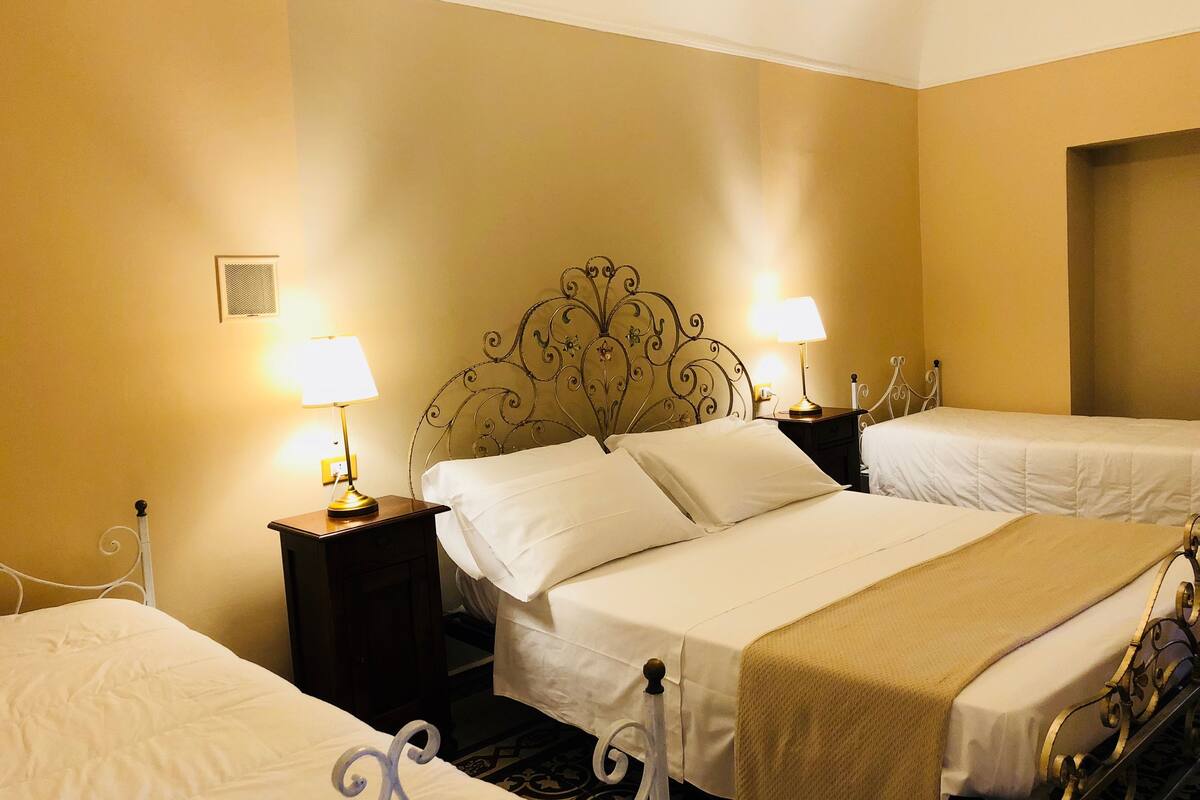 Habitación de hotel con dos camas, cada una con una colcha blanca y una lámpara dorada.