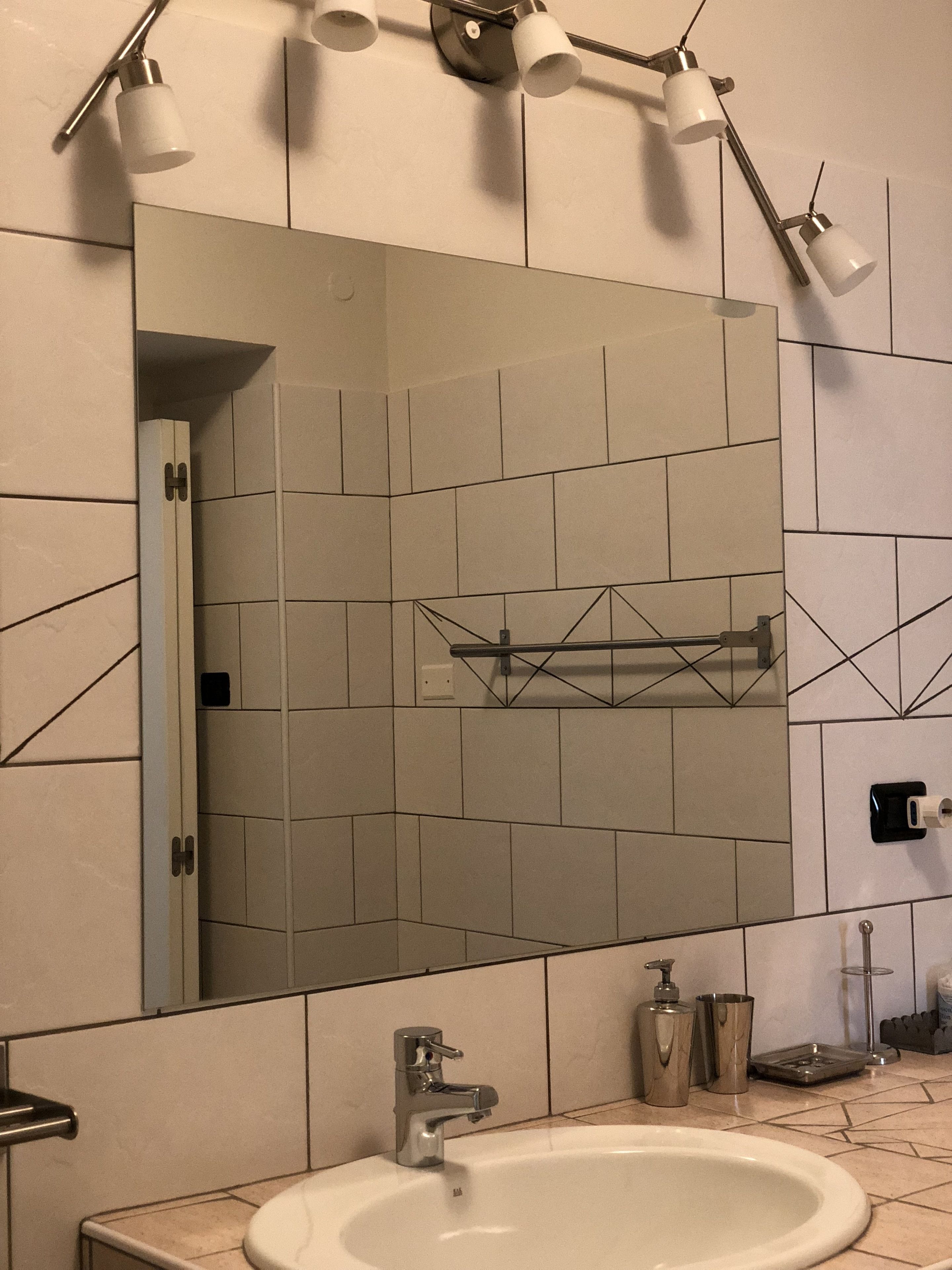 A bathroom with a large mirror, a sink, and a towel rack.