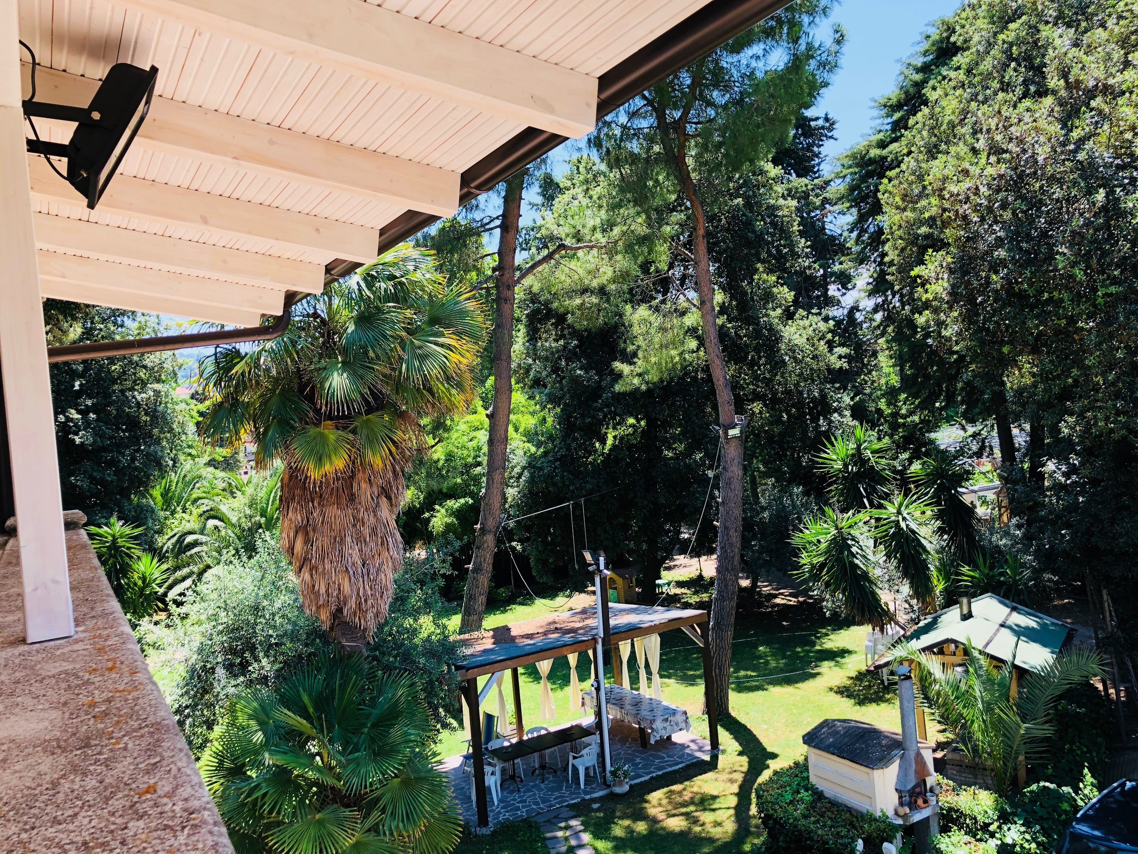 Een overdekt buitengebied met een houten pergola, een tafel met stoelen en een klein gebouw met schoorsteen.
