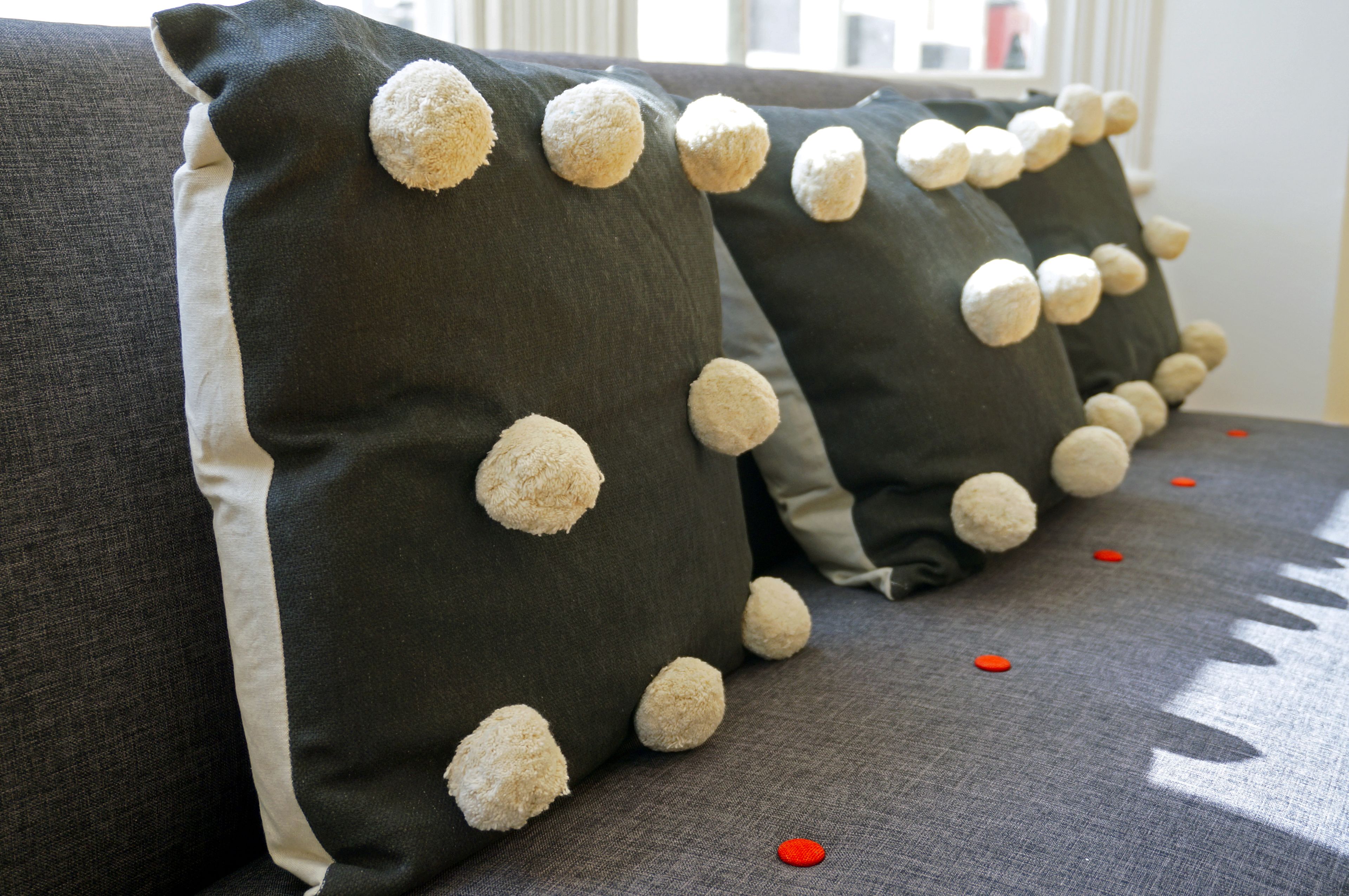 Una hilera de sofás grises con almohadones blancos y negros que tienen pompones blancos.