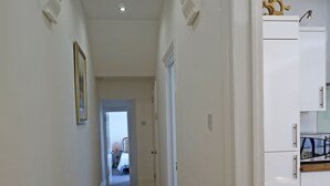 Corredor com piso de madeira, paredes brancas e teto com iluminação embutida. Uma porta dá acesso a outro cômodo.