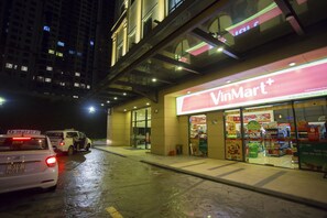 Vista nocturna de una tienda VinMart con pavimento mojado, coches estacionados aledaños y un edificio de varios pisos al fondo.