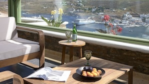 A balcony with a view of a coastal town, a table with a bowl of fruit, a bottle, and a glass. - EmGard Suites Kythnos (Kithnos)