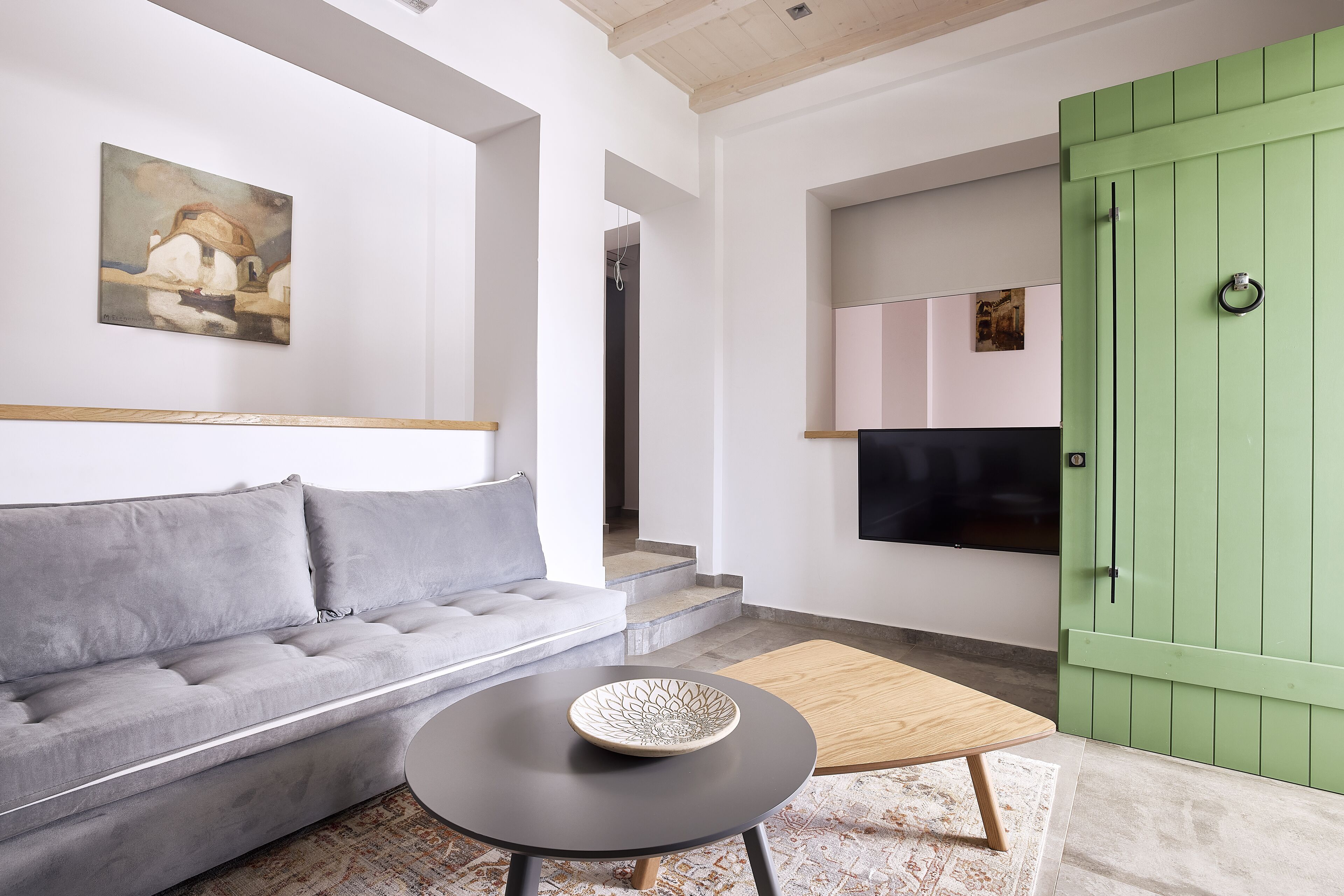 Una sala moderna con un sofá gris, una mesa redonda negra con un cuenco decorativo y una puerta verde.