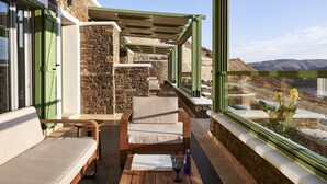 A balcony with a wooden bench, a table with a book and a bottle, and a view of a mountainous landscape. - EmGard Suites Kythnos (Kithnos)