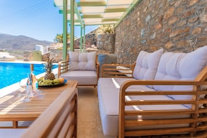 A poolside area with wooden lounge chairs and a table, a bottle of champagne, and a fruit bowl. - EmGard Suites Kythnos (Kithnos)
