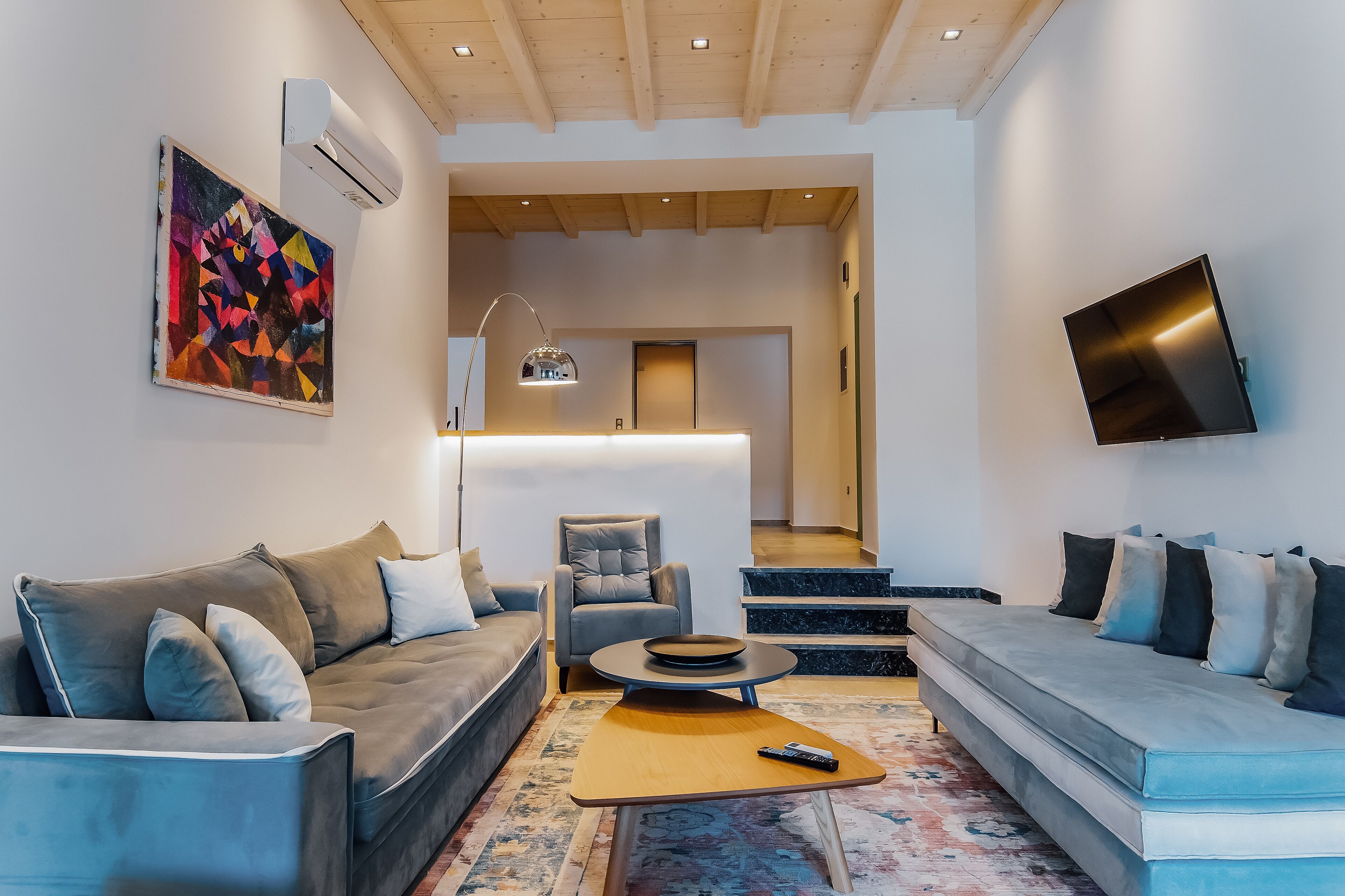 A modern living room with a sofa, armchair, and a flat-screen TV mounted on the wall.