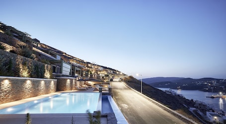 A hillside hotel with a swimming pool, outdoor seating, and a view of the sea.