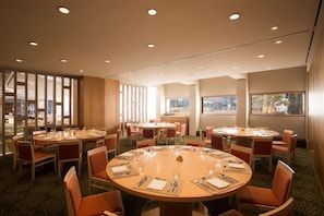 A hotel conference room with multiple round tables, each set with chairs and dining essentials.
