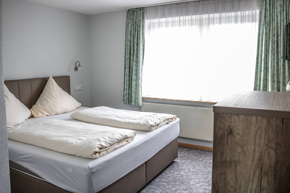 A double bed with a headboard, a bedside table, and a window with curtains.