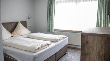 A double bed with a headboard, a bedside table, and a window with curtains.