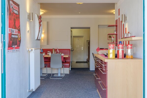 A hotel corridor with a red booth seating area, a counter with dispensers, and a poster on the wall.